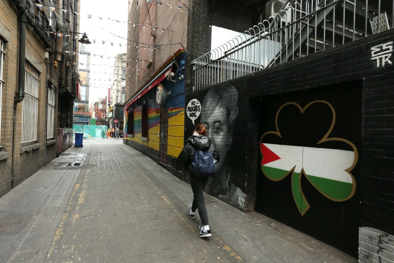 Dublin, Irlande - 21 mars 2025 - Une femme passe devant une fresque murale représentant un trèfle avec le drapeau palestinien sur Dame Lane, dans le centre de Dublin.